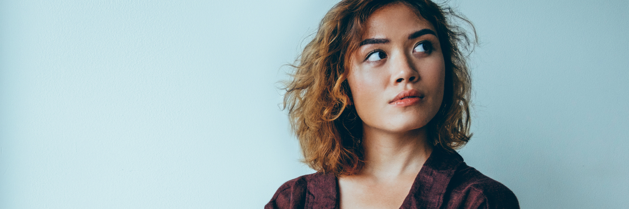Why Naming Your Mental Health Can Be Powerful Portrait of pensive young Asian woman wearing oversized shirt standing with crossed arms and looking away.