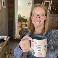 Photo of woman wearing glasses and holding a mug that says "strong vibes calm mind"