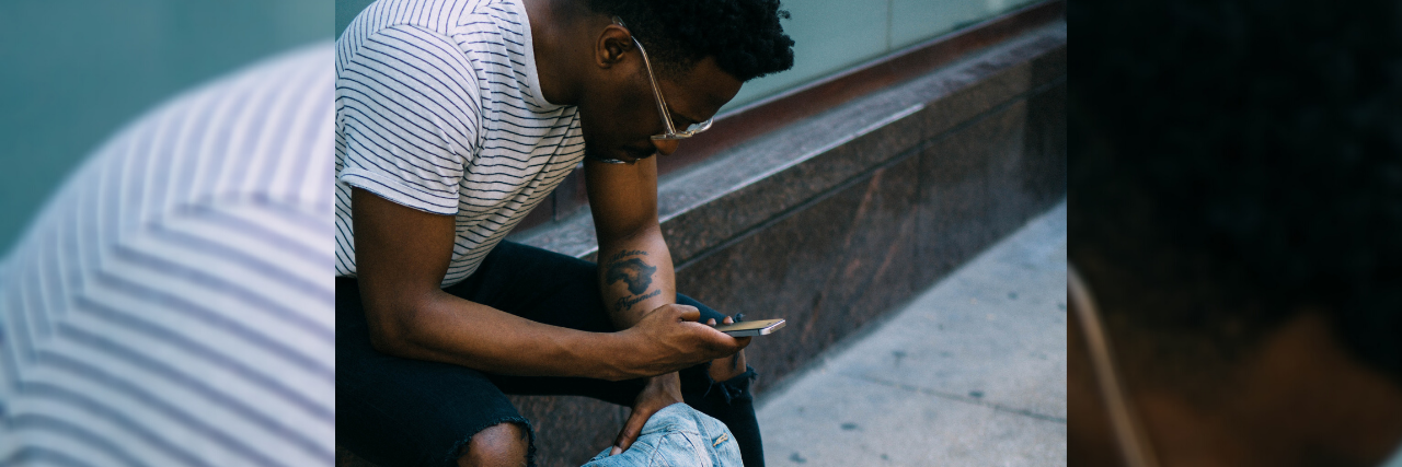 3 Ways to Stop ‘Doomscrolling’ for Your Mental Health This Week photo of a man leaning on shop window front, checking his phone and holding a denim jacket