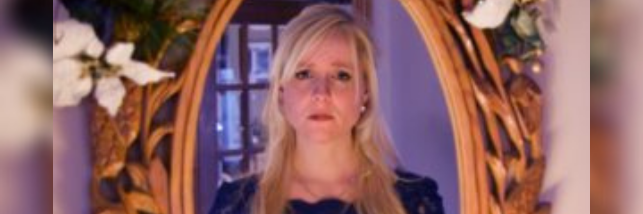 My Experience With Benzodiazepine Addiction After My Mom's Suicide photo of author, a white woman with long blonde hair looking into a gold oval mirror with a straight face