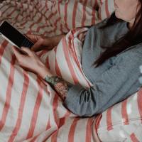 a woman sitting in bed looking at her phone