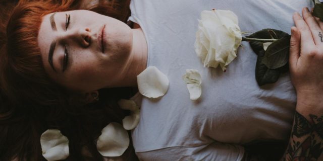 woman sleeping or lying down with her eyes closed, a rose on her chest, photo taken from above