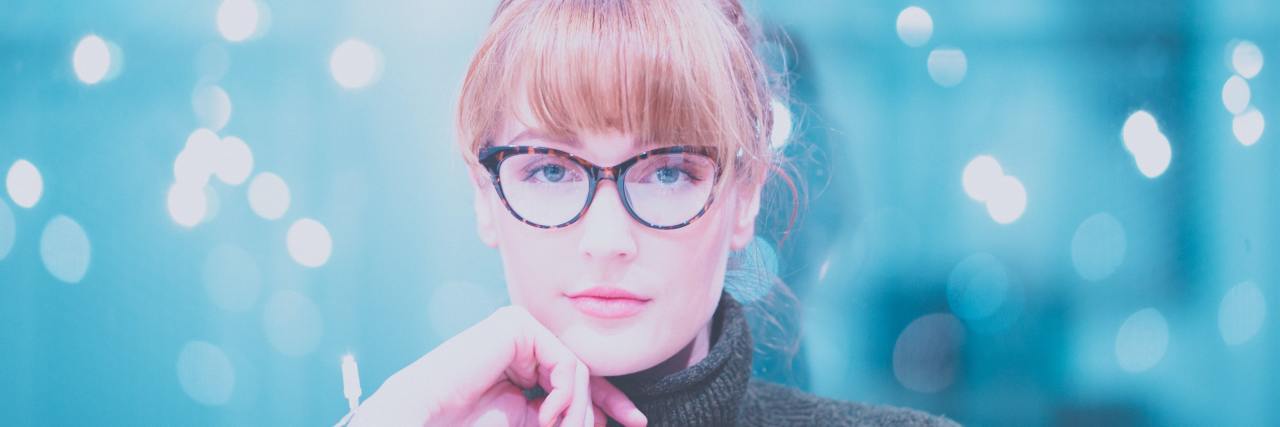 How Schizophrenia Helped Me Find My Purpose in Helping Others woman in glasses and a dark gray turtleneck looking at camera contemplatively with a hand on her chin