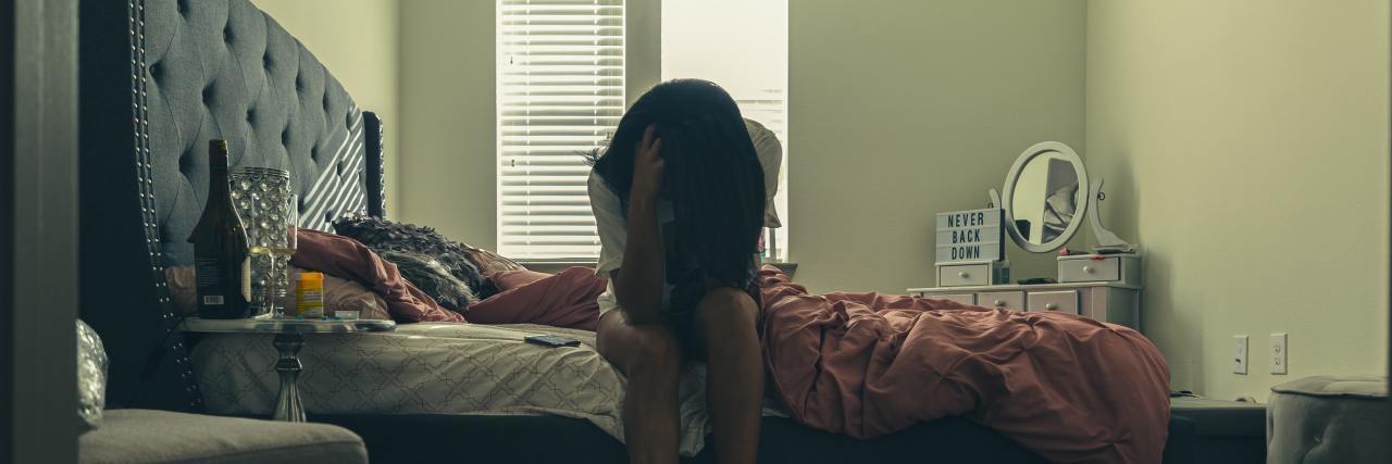 When I Missed My Depression Medication When I Was Feeling Well photo of woman sitting on the bed of a bed, head in her hands, with medication on bedside table