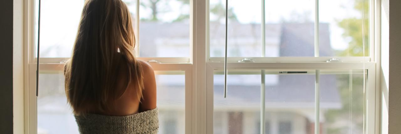 COVID-19 Isolation Survival Tips After Possible Exposure photo of woman looking out of window at houses and garden, wrapped in a sheet or towel