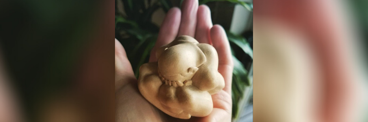 Photo of hands holding a small "buddha weeps" statue
