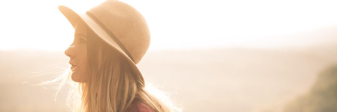 Side profile of a young white woman in a sun hat outside on a sunny day