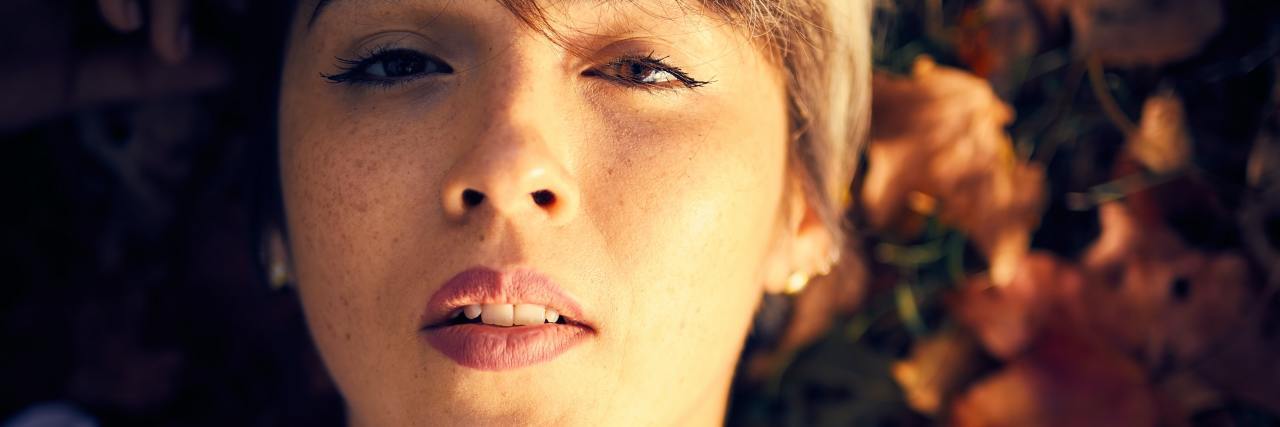 What It's Like to Have a Rare, Orphan Disease A woman with short hair and a white shirt looking up, laying on a pile of leaves