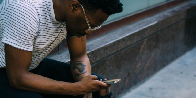 3 Ways to Stop ‘Doomscrolling’ for Your Mental Health This Week photo of a man leaning on shop window front, checking his phone and holding a denim jacket