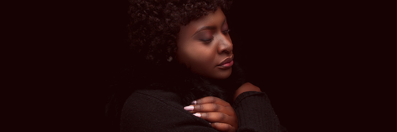 photo of a woman with her eyes closed, arms crossed on her chest, looking thoughtful