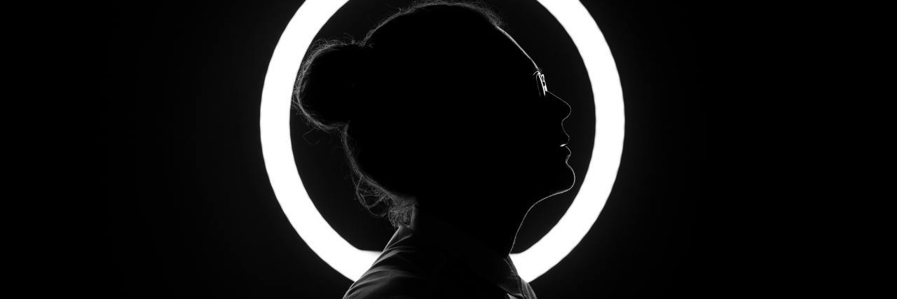 black and white photo of woman in silhouette in front of a circular ring of white light