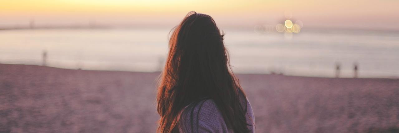 How I Learned to Finally Let Go and Grieve After a Traumatic Death A woman in a sweater with long, brown hair walking on the beach at sunset