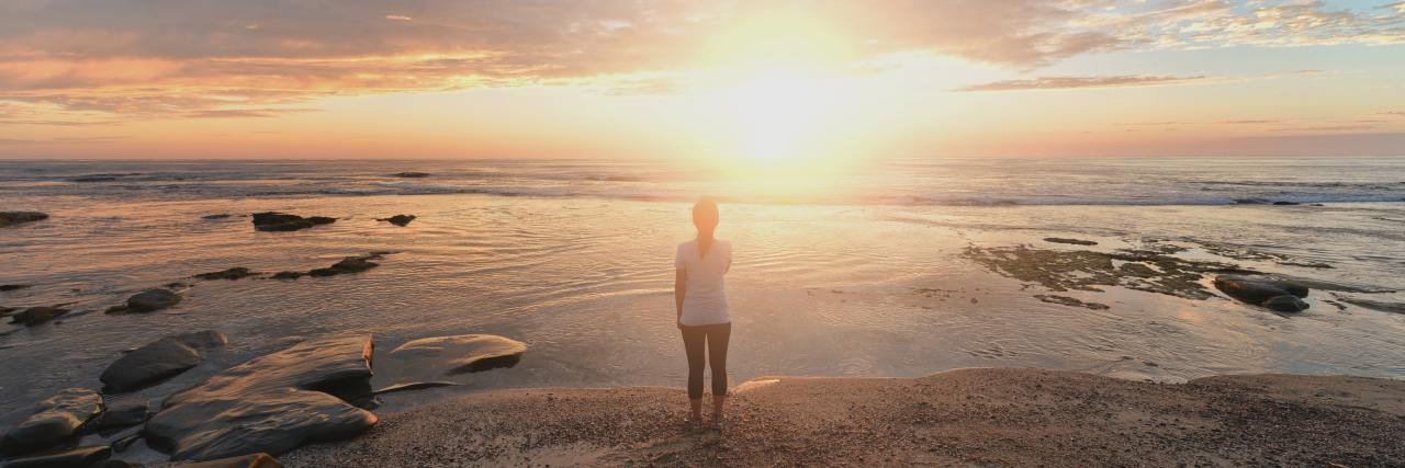 photo of woman on shoreline looking out to sea at sunrise