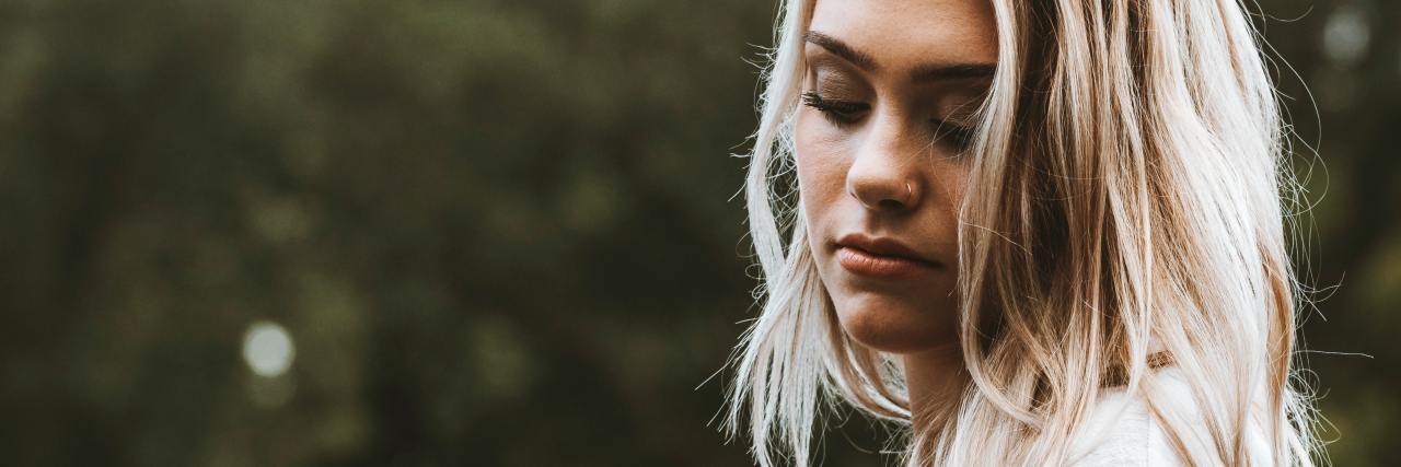 Depression Always Seems to Win Its Battles photo of woman with her eyes closed and head bowed, posed in profile against blurry trees background