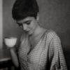 black and white photo of woman with short hair holding a cup and looking down