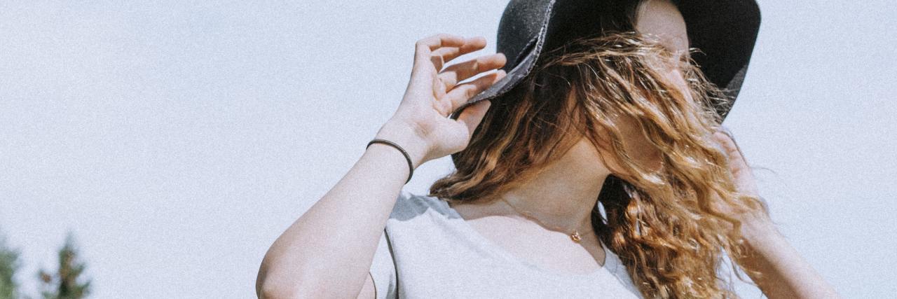 Borderline Personality Disorder and Radical Acceptance During COVID-19 photo of woman wearing a hat, her face partly covered by her hair, looking away from camera with trees in the background