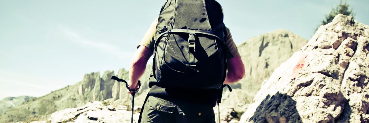 How I Conquered My Anxiety of Hiking Alone photo of a man hiking up a hill with a backpack and hiking poles