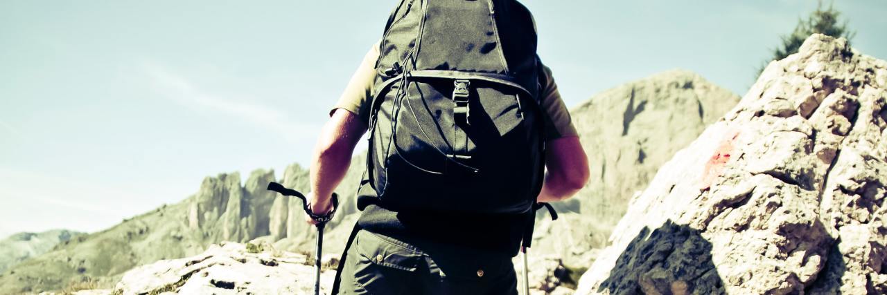 photo of a man hiking up a hill with a backpack and hiking poles