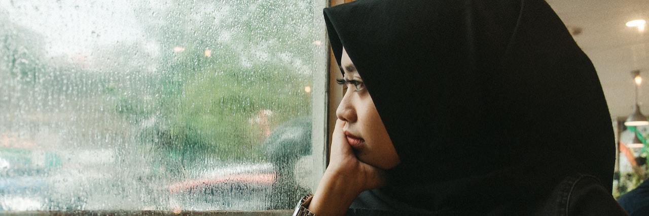 People With Schizophrenia May Have Higher COVID-19 Risk Woman wearing a hijab looks out a window into a rainy landscape with a cup of coffee in front of her