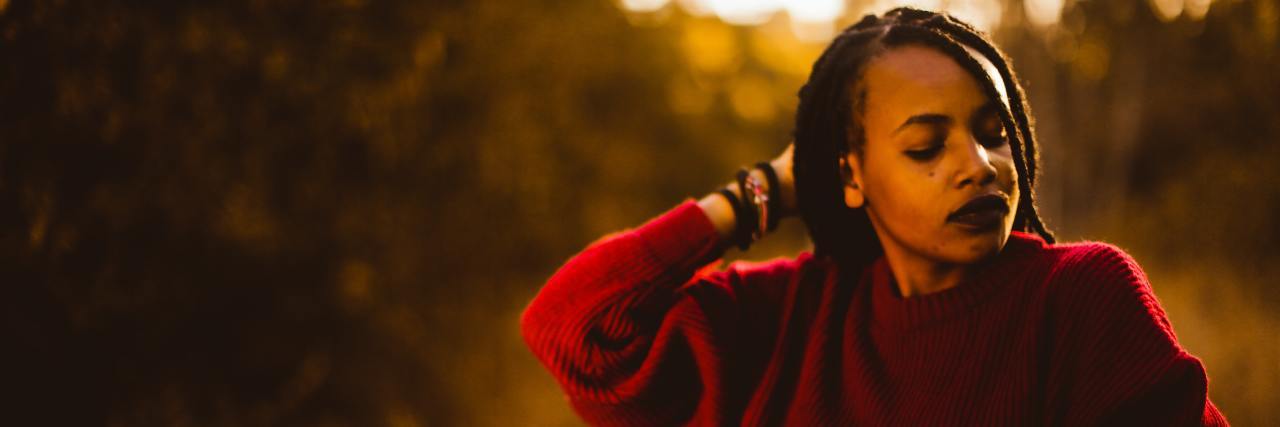 Black woman on a trail in a red sweater, eyes closed, hand behind her head