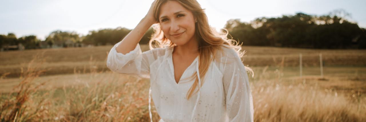 It's OK to Relapse in Mental Health Recovery During COVID-19 photo of woman in countryside silhoutted by the sun, looking into the camera and smiling with her hand in her hair