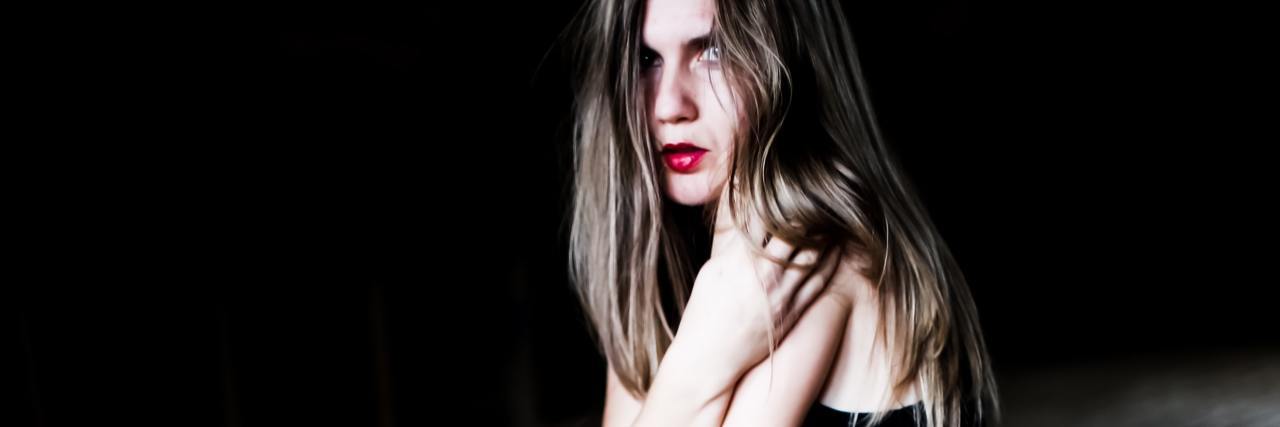 How to Help Someone With Paranoid Delusions in the Workplace photo of woman looking scared, holding her arms close to her, while kneeling on wooden floor and looking into camera
