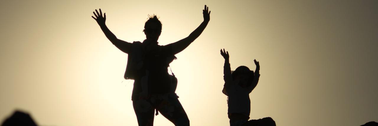 How Bipolar Disorder Makes Me a Better Parent to My Complex Needs Kids photo of mother and child having fun with arms raised, silhouetted against featureless sky at sunset
