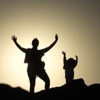 photo of mother and child having fun with arms raised, silhouetted against featureless sky at sunset
