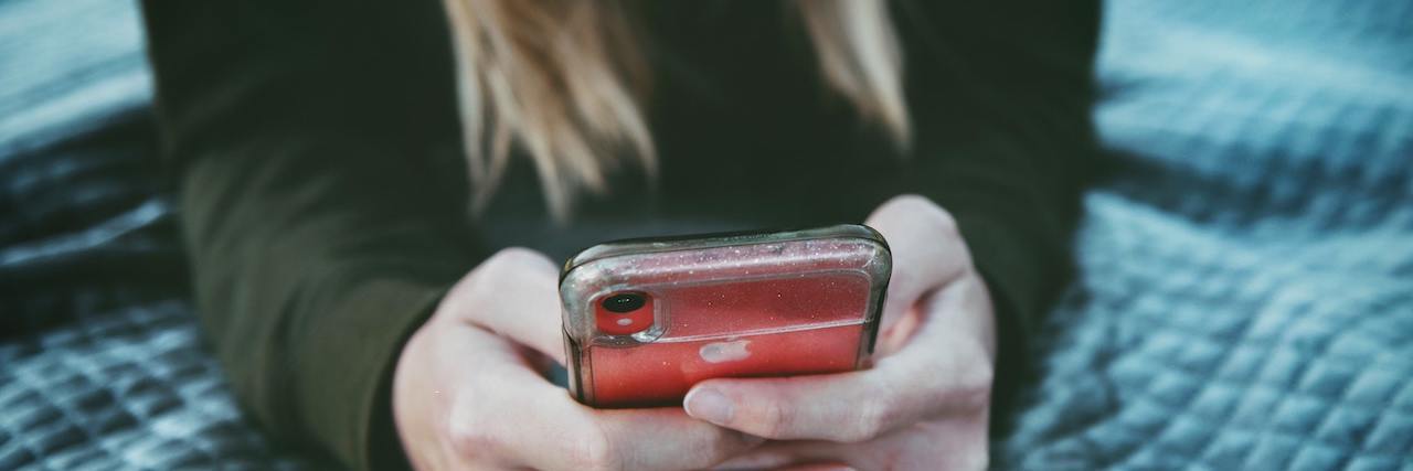 What It's Like to Have Severe Relationship Anxiety woman lying on her bed holding a phone, appearing to be texting