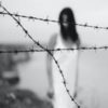 black and white photo of woman blurred behind clear image of barbed wire