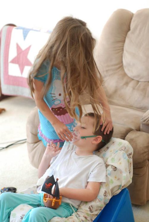 Sister helping brother with breathing treatments.