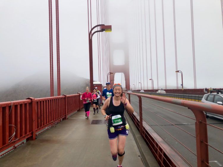 photo of the contributor running across the Golden Gate Bridge during the San Francisco marathon in 2018, smiling and waving fo the camera