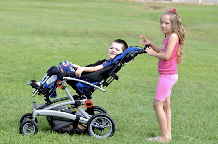 Lori's daughter pushing her son outdoors in his wheelchair.