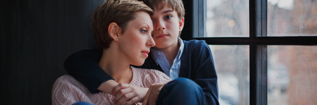 Pandemic Parenting with Mental Illness a young teen boy hugging his mom as she looks out the window