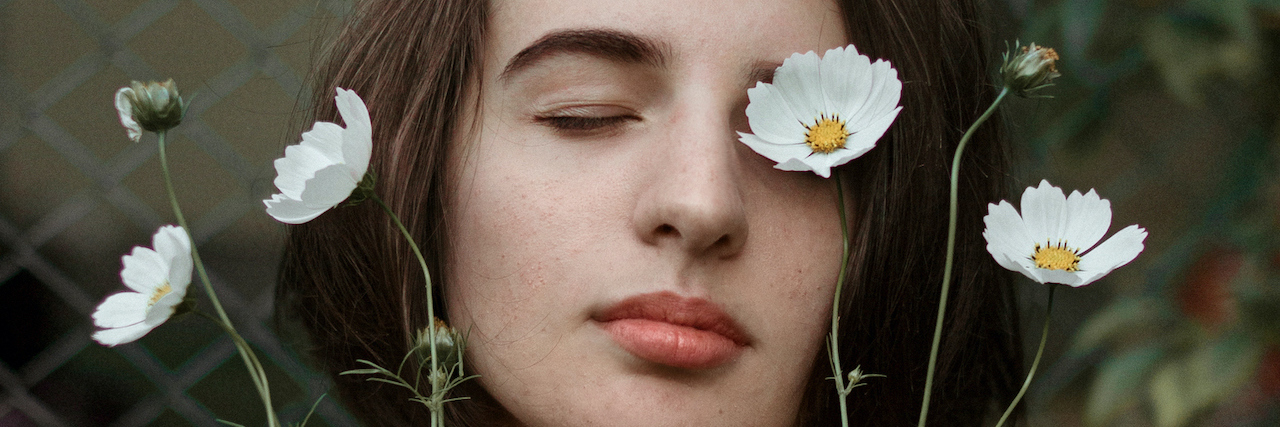 A woman with flowers in front of her face. She's closing her eyes