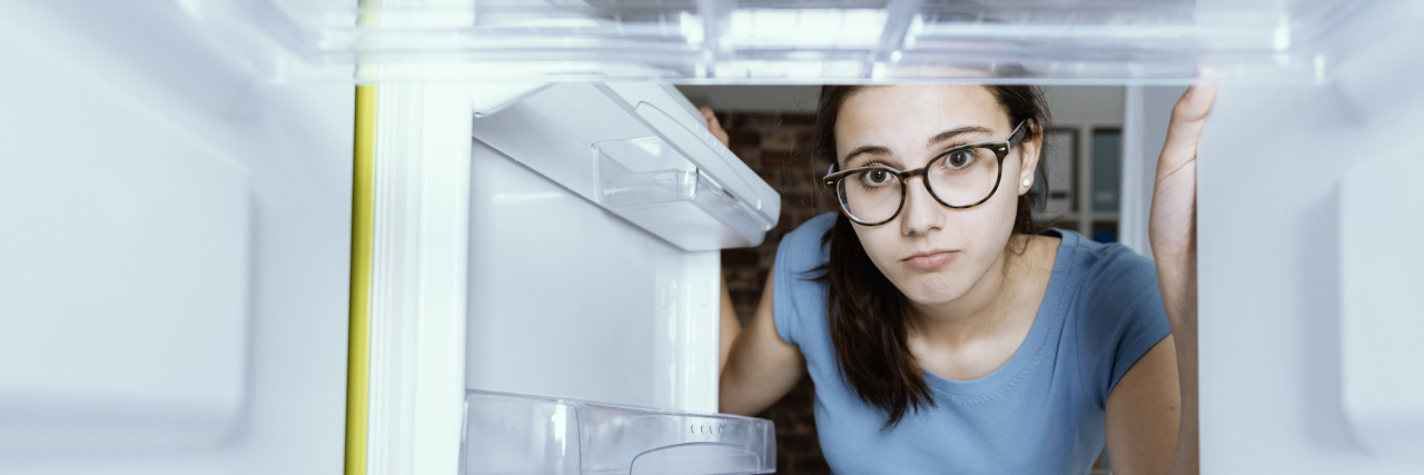 young white woman with glasses looking inside an empty fridge