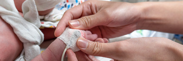 Mother holding baby's hand in NICU.