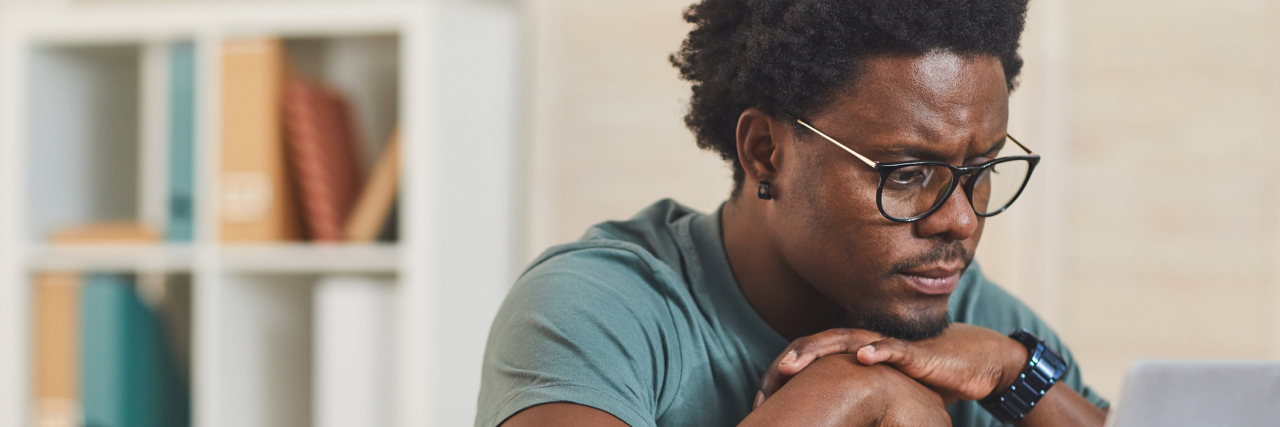 Can People With ADHD Experience Hyperfixation young man in eyeglasses sitting at the table in front of laptop computer and looking at monitor