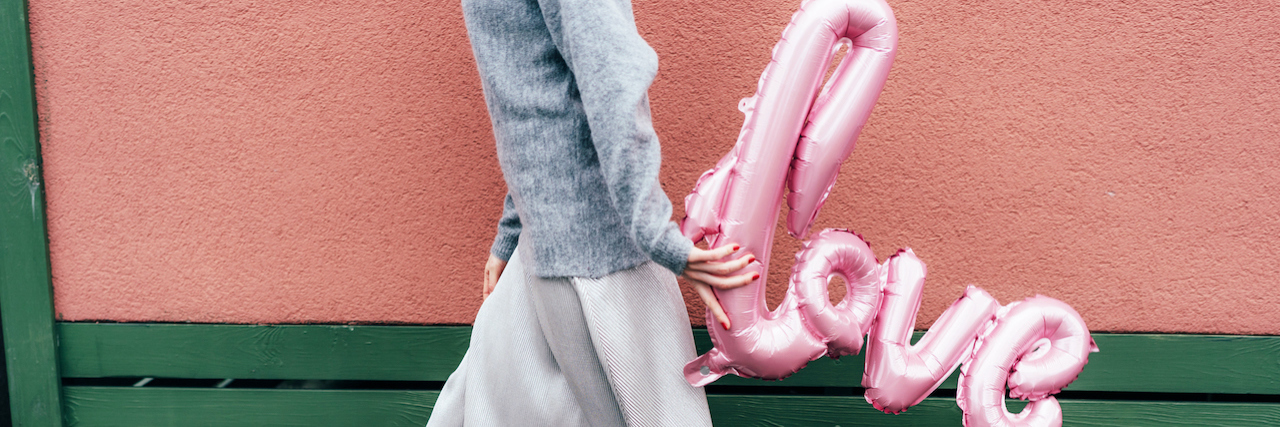 Stylish female figure with a skirt walks and carries the inflatable pink word LOVE