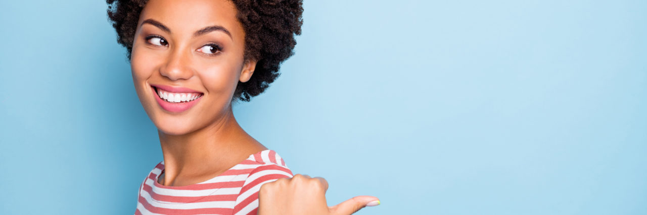 10 Surprisingly Great Things About Having Ulcerative Colitis Woman wearing a red and white striped shirt points behind herself with a thumb