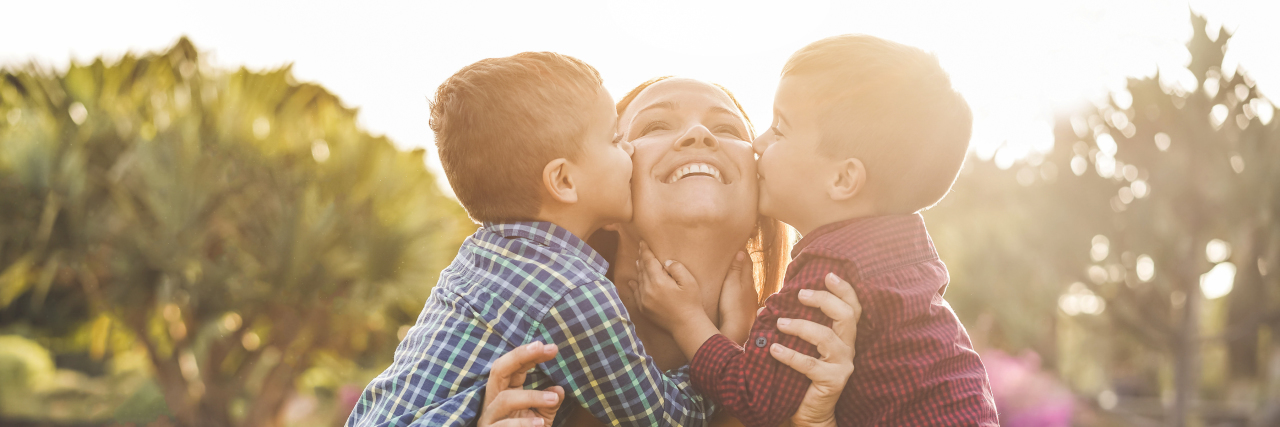 Our World of Small Miracles Raising Twins With Autism Mother with twin sons kissing her cheeks.