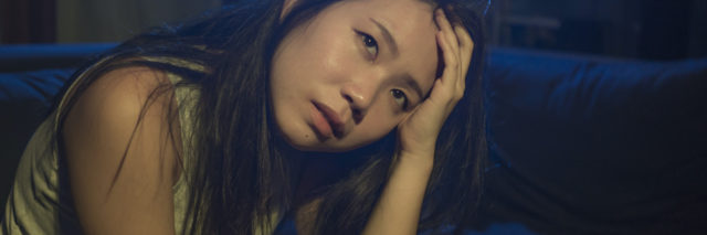 An asian American woman sitting on a couch looking up, with a saddened expression on her face
