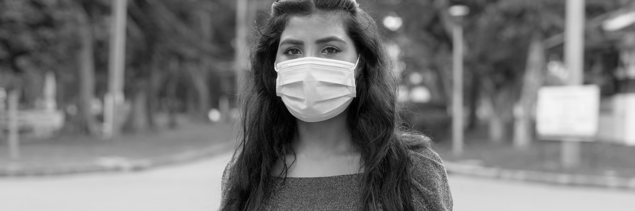 black and white photo of woman wearing a face mask looking into the camera with a serious expression