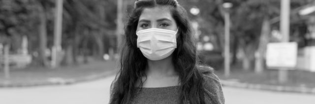 black and white photo of woman wearing a face mask looking into the camera with a serious expression