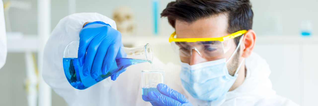 A white male scientist with goggles and a mask mixing chemicals in a test tube