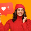 Woman wearing a red sweater and red beanie holding up a posted on a heart/like button from social media