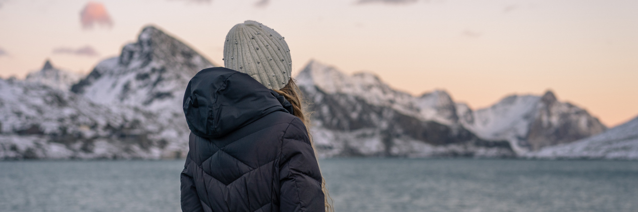 My Journey With What It's Like to Live With OCD A young woman in a black winter coat, looking out at the ocean with snowy mountains in the distance