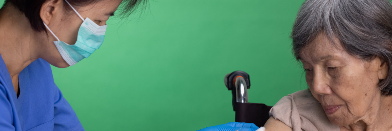 What's the Difference Between Vaccine Hesitancy and Vaccine Refusal? nurse giving vaccine injection to senior woman.