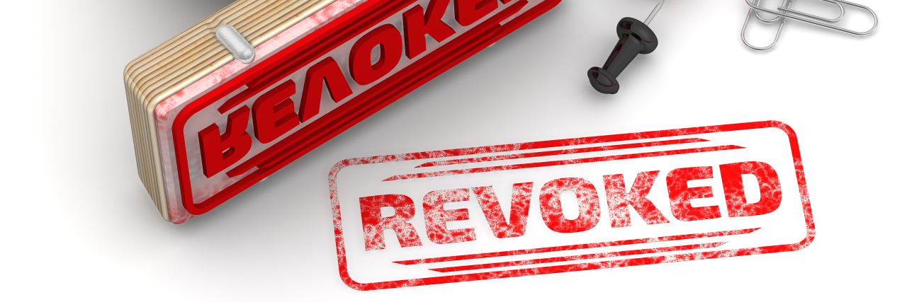 When My Long-Term Disability Was Revoked Because I 'Don't Look Sick' Wooden stamp and red imprint REVOKED on white surface.