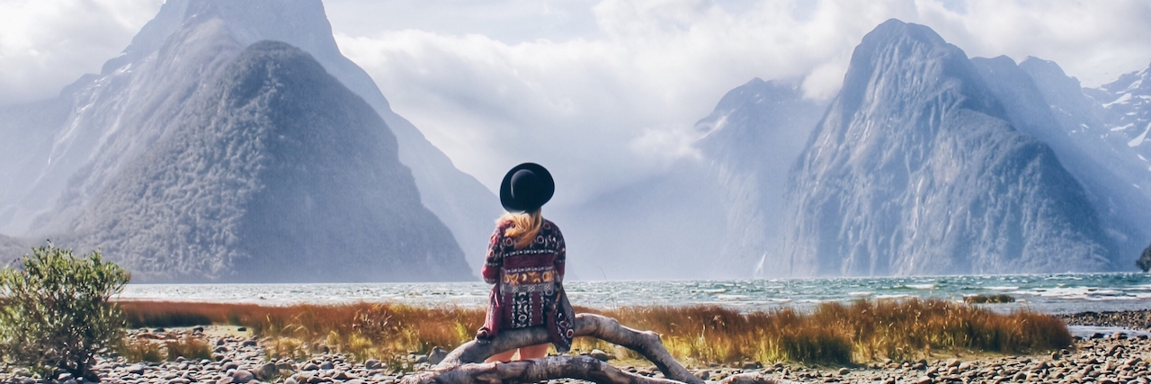Woman sitting on driftwood lakeshore against snowcapped mountains in New Zealand